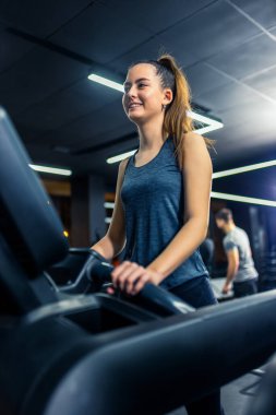 Kız spor salonunda koşu bandında koşuyor.
