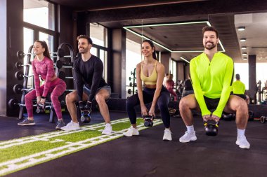 Bir grup insan dambıllarıyla ağırlıklı çömelme hareketleri yapıyor..