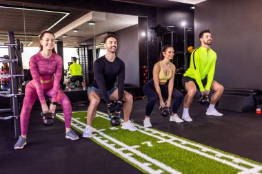 Bir grup insan dambıllarıyla ağırlıklı çömelme hareketleri yapıyor..