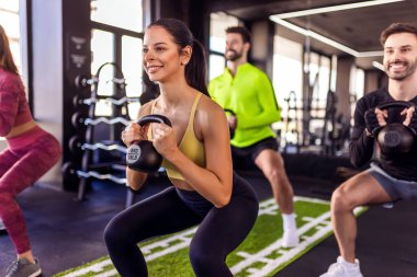 Bir grup insan dambıllarıyla ağırlıklı çömelme hareketleri yapıyor..