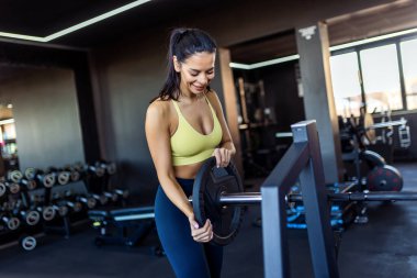 Genç, formda bir kadın spor salonundaki bir bara ağırlık veriyor..