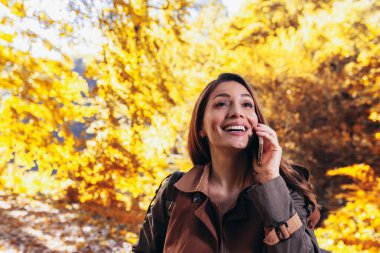 Sonbahar parkında telefonunu kullanan mutlu genç bir kadın..