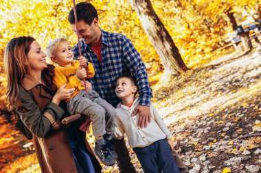 Mutlu aile sonbahar parkında salıncakta sallanırken eğleniyor..