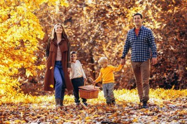 Mutlu bir aile ve iki küçük oğlu parkta rahat bir sonbahar pikniği yapıyorlar..
