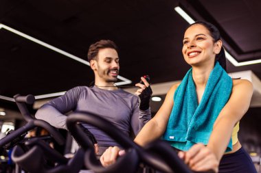Spor salonunda özel antrenörü onu cesaretlendirirken bisiklet süren bir kadın..