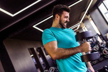 Spor salonunda silah eğitmek için dambıl kullanan zinde bir adam..