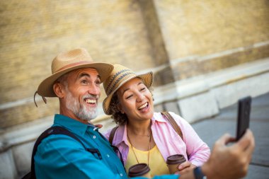 Yaşlı evli bir çift kahveyle selfie çekiyor. Yeni şehri keşfeden turistler.