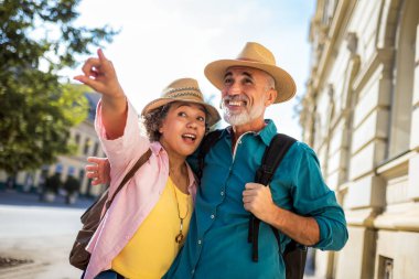 Yeni şehri keşfeden yaşlı evli bir çift. Şapka ve sırt çantası takıyorlar..