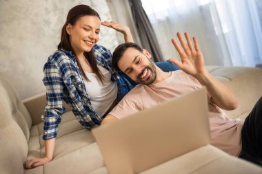 Evlerindeki koltukta oturan çift laptoplarıyla görüntülü konuşuyorlar..