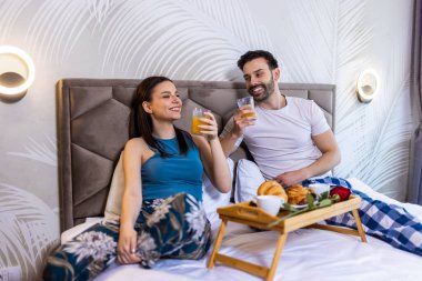 Tatlı çift yatakta kahvaltı yapıyor. Kahve içiyorlar ve sabahları eğleniyorlar..