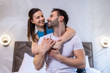 Genç mutlu çift yatakta. Kız arkadaşı erkek arkadaşına arkadan sarılıyor. Birbirlerine bakıyorlar..