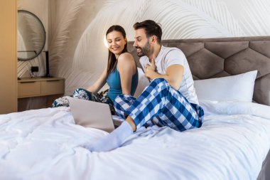 Yatakta pijamalı bir çift laptoplarını kullanıyor..