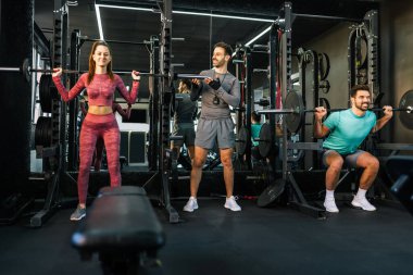 Grup çalışması. İki müşteriyle kişisel antrenör halterde çömelme yapıyor..