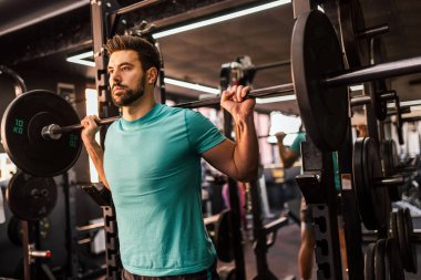Atletik adam spor salonunda halterle çömeliyor..