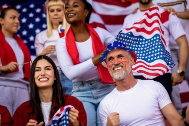 Amerikan futbolu ve futbol taraftarları stadyumda bayrak ve diğer ekipmanlarla tezahürat yapıyorlar.