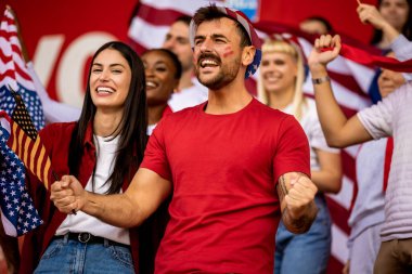 Amerikan futbolu ve futbol taraftarları stadyumda bayrak ve diğer ekipmanlarla tezahürat yapıyorlar.