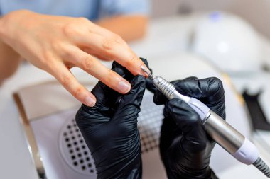 Güzellik salonunda elektrikli makine kullanan profesyonel bir manikürcü. Güzellik salonunda tırnaklarını yaptıran bir kadın..