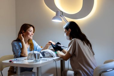 Güzellik salonunda elektrikli makine kullanan profesyonel bir manikürcü. Güzellik salonunda tırnaklarını yaptıran bir kadın..