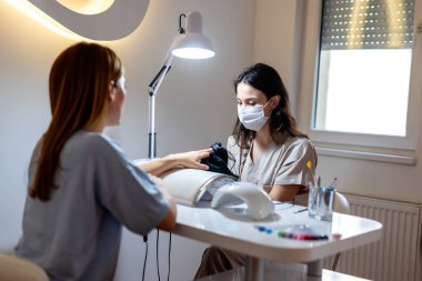 Güzellik salonunda elektrikli makine kullanan profesyonel bir manikürcü. Güzellik salonunda tırnaklarını yaptıran bir kadın..