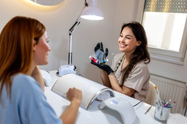 Müşteri jel cilası için tırnak rengini seçiyor. Profesyonel manikür ona yardımcı olur..