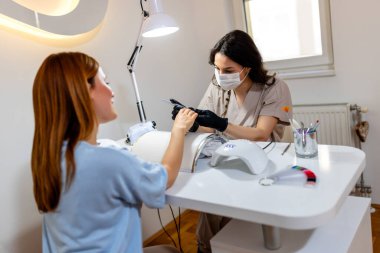 Manikürcü müşterinin tırnaklarını güzellik salonunda törpülüyor..