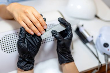 Manikürcü müşterinin tırnaklarını güzellik salonunda törpülüyor..