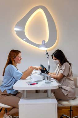 Manikürcü müşterinin tırnaklarını güzellik salonunda törpülüyor..