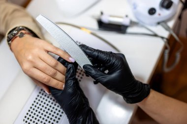 Manikürcü müşterinin tırnaklarını güzellik salonunda törpülüyor..