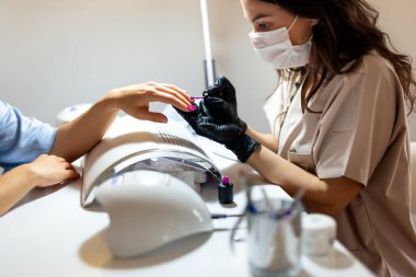 Güzellik uzmanı müşterisinin tırnaklarına oje sürüyor. Lüks güzellik salonunda profesyonel manikür..