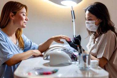 Güzellik uzmanı müşterisinin tırnaklarına oje sürüyor. Lüks güzellik salonunda profesyonel manikür..