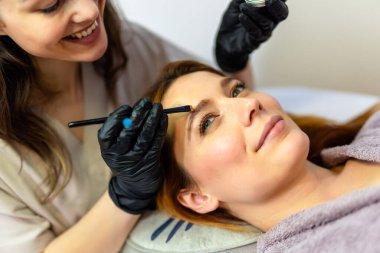 Güzellik uzmanı, kaş boyası sürerken bir kadının kaşlarına ince bir fırça kullanıyor..