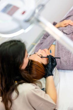 Güzellik uzmanı, kaş boyası sürerken bir kadının kaşlarına ince bir fırça kullanıyor..