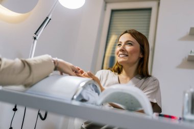 Güzellik salonunda elektrikli makine kullanan profesyonel bir manikürcü. Güzellik salonunda tırnaklarını yaptıran bir kadın..