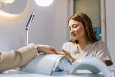 Güzellik salonunda elektrikli makine kullanan profesyonel bir manikürcü. Güzellik salonunda tırnaklarını yaptıran bir kadın..