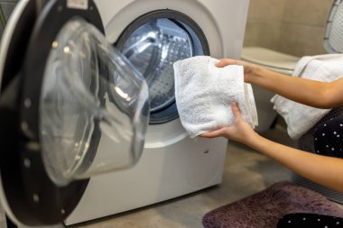 Kadın çamaşır makinesine havlu koyar.. 