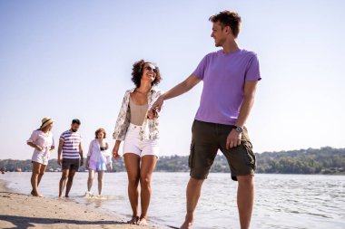 Genç bir çift kumsalda yürüyor, arkadaşlıklarından ve dalgaların sesinden keyif alıyorlar. El ele tutuşup gülümserler. Sahilde huzurlu ve romantik bir an yaşarlar..