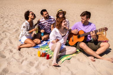 Sıcak bir yaz günü plajda dinlenen bir grup genç arkadaş. Bir adam gitar çalarken diğerleri renkli kokteyllerin tadını çıkarıyor, gülüyor ve güneşte ıslanıyor..