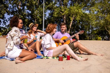 Sıcak bir yaz günü plajda dinlenen bir grup genç arkadaş. Bir adam gitar çalarken diğerleri renkli kokteyllerin tadını çıkarıyor, gülüyor ve güneşte ıslanıyor..