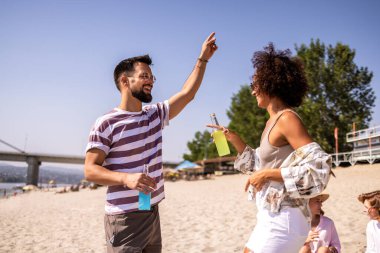 Canlı bir plaj partisinde kokteyl içen bir grup arkadaş. Arka planda müzik, renkli içecekler ve okyanusun üzerinde güneş batarken sahne enerji, eğlence ve yaz kutlamalarıyla dolu. Saf sahil titreşimleri ve gençlik sevinci.