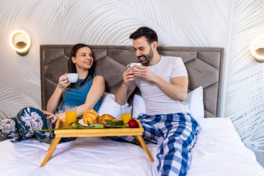 Tatlı çift yatakta kahvaltı yapıyor. Kahve içiyorlar ve sabahları eğleniyorlar..