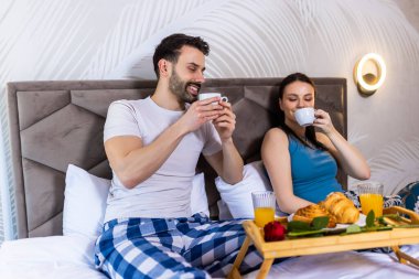 Tatlı çift yatakta kahvaltı yapıyor. Kahve içiyorlar ve sabahları eğleniyorlar..