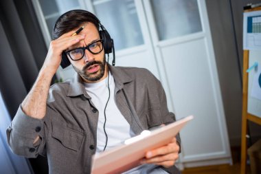 Masasında oturan genç adam, hayal kırıklığı içinde başını tutuyor ya da not defterine bakarken strese giriyor..