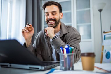 Modern, rahat bir ev ortamında dizüstü bilgisayarıyla çalışan genç bir adam..
