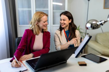 Ev ofisinde birlikte çalışan iki genç kadın, bir dizüstü bilgisayara odaklanmış.