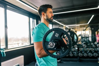 Atletik adam spor salonunda halterle çömeliyor..