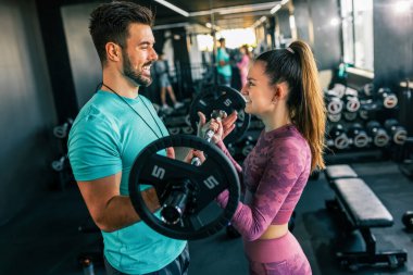 Genç bir kadın spor salonunda ağırlıklarla omuz presi yaparken antrenörü onu fark ediyor..