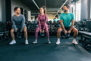 Modern bir spor salonunda iki erkek ve bir kadın ağırlık kaldırıyor.. 