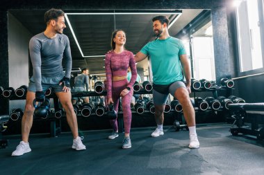 Modern bir spor salonunda iki erkek ve bir kadın ağırlık kaldırıyor.. 