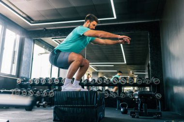 Modern bir spor salonunda yapılan yoğun bir çalışma sırasında zıplarken yakalanan zinde genç bir adam..