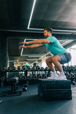 Modern bir spor salonunda yapılan yoğun bir çalışma sırasında zıplarken yakalanan zinde genç bir adam..